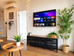 A living room with a mounted TV displaying streaming services, a wooden console table with plants, and a remote control on a side table. - Downtown Penthouse - Free Indoor Parking, Balcony, Terrace, Gym (Québec)