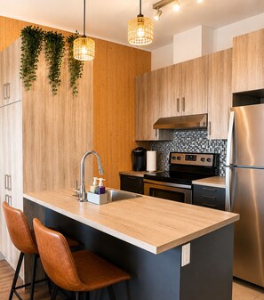 A modern kitchen with a central island, stainless steel appliances, and wooden cabinetry. - Downtown Penthouse - Free Indoor Parking, Balcony, Terrace, Gym (Québec)