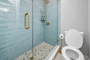 Ein Badezimmer mit Duschkabine aus Glas, einer weißen Toilette und Fliesenboden.