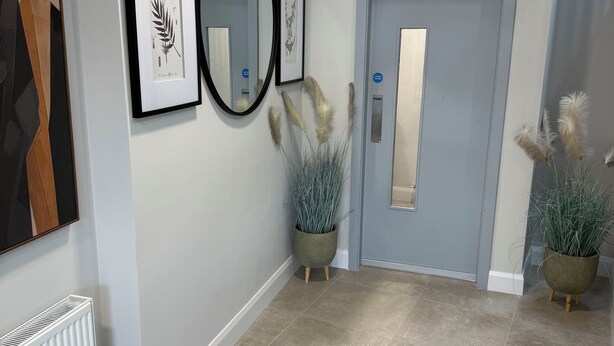 A hallway with framed botanical prints, a mirror, a door, and potted plants.