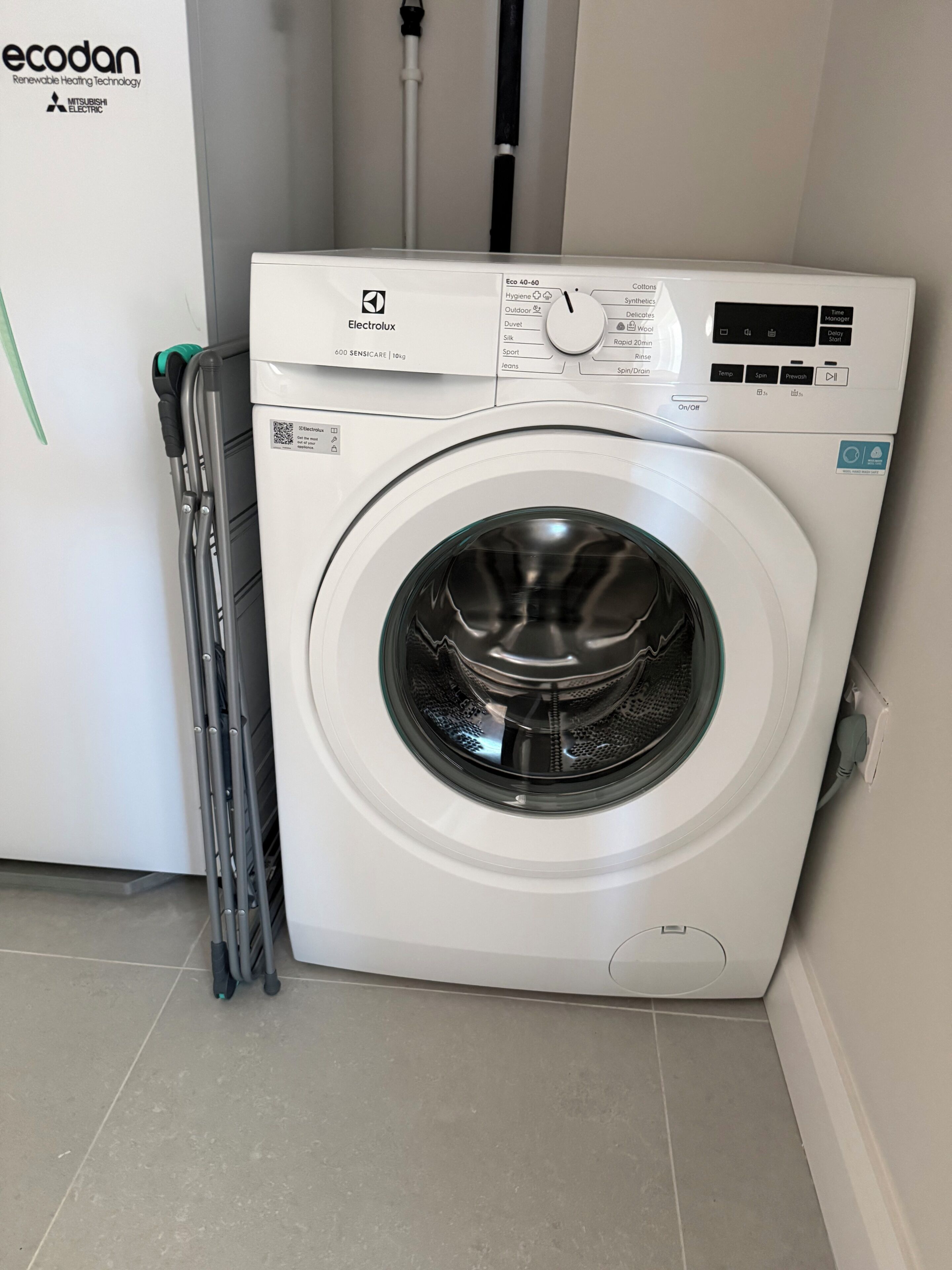 Máquina de lavar frontal com painel de controle, um código QR e uma etiqueta indicando que é o modelo 600 SENSICARE 10kg.