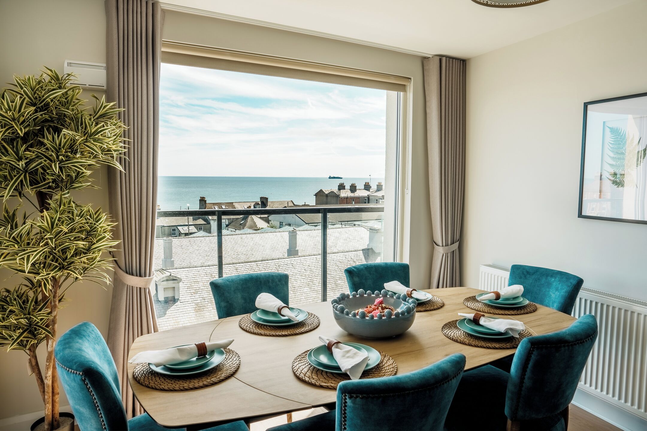 A dining area with a view of the sea, a potted plant, and a table set for four.