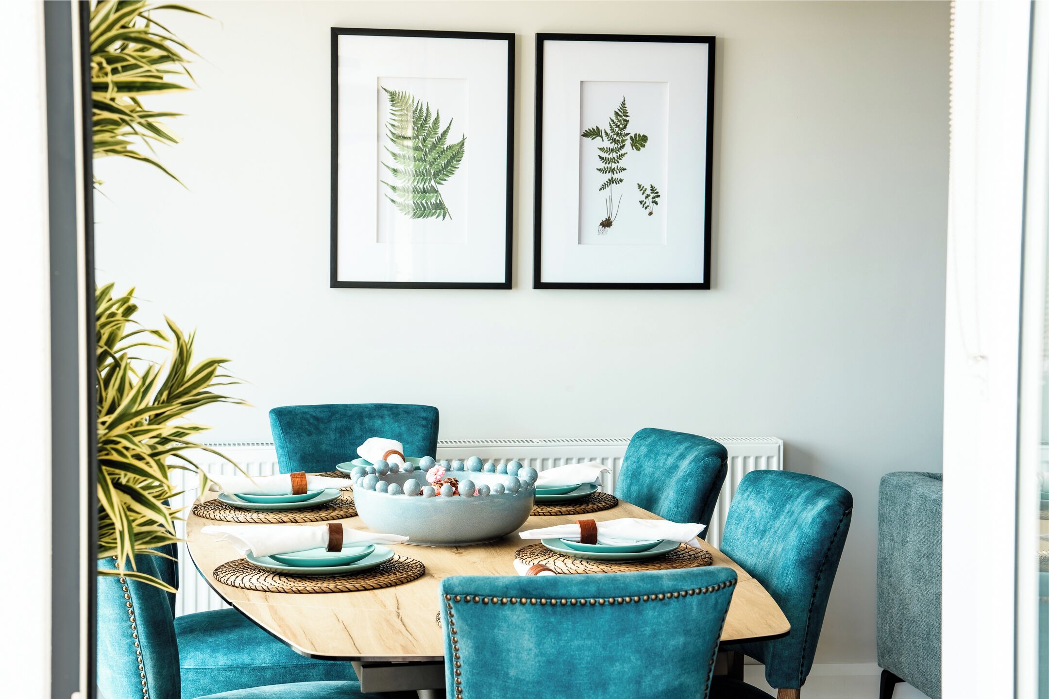 Een eetgedeelte met teal stoelen, een ronde tafel en een schaal decoratieve objecten.