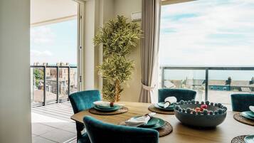 Un comedor con una mesa dispuesta para cuatro, una planta en maceta y vistas de la ciudad a través de grandes ventanales.