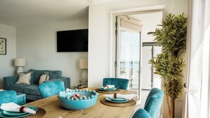 A modern living room with a teal sofa, a dining table with blue plates, and a large plant.