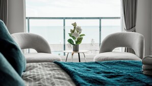 A hotel room with a bed, two chairs, a small table, and a view of the sea.