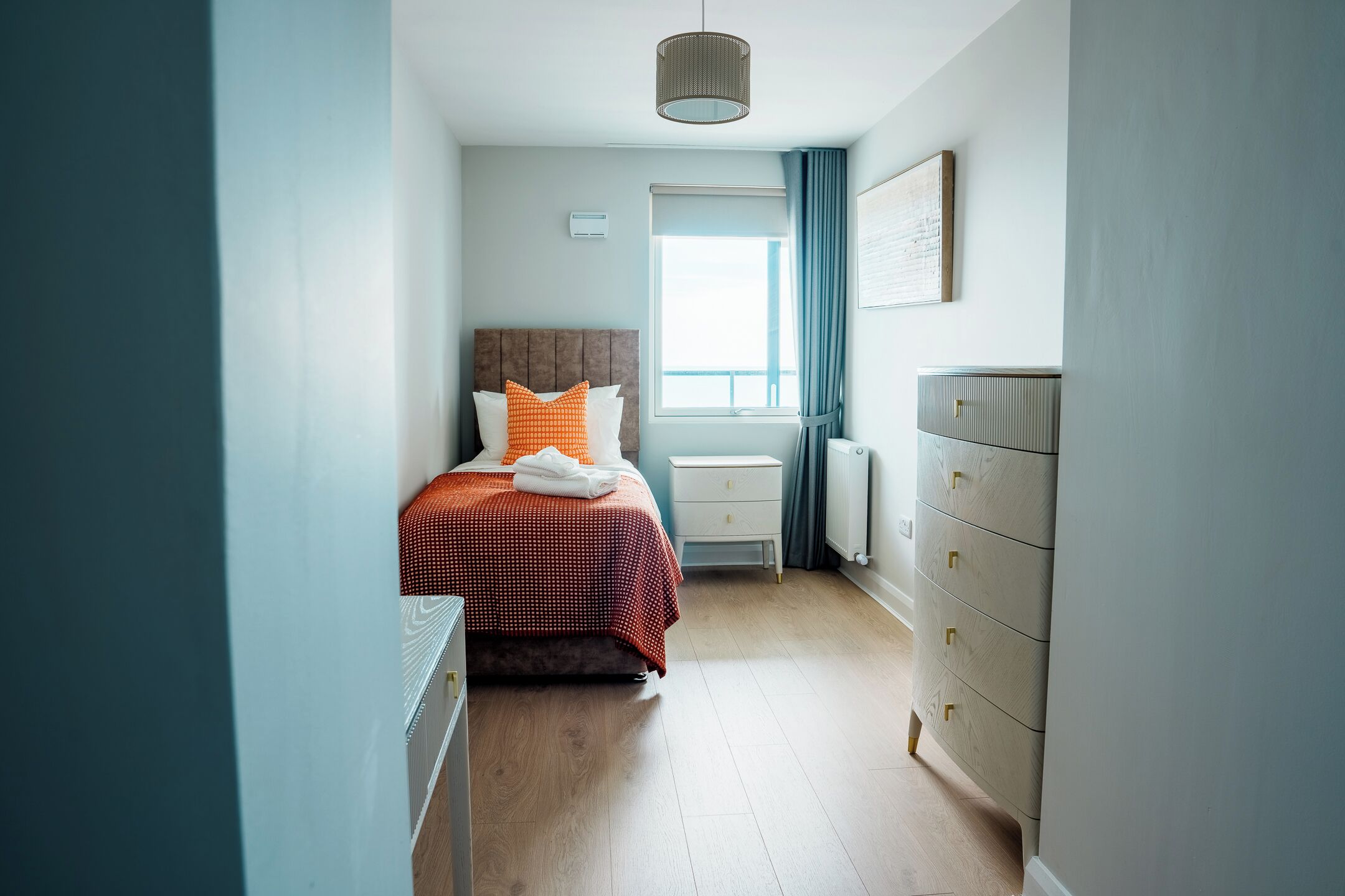 A bedroom with a bed, bedside tables, a radiator, and a window with curtains.