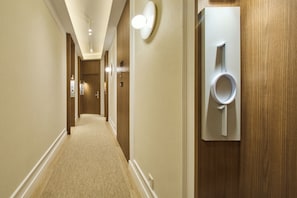 Pasillo de hotel con piso alfombrado, puertas de madera y luminarias fijadas a la pared.