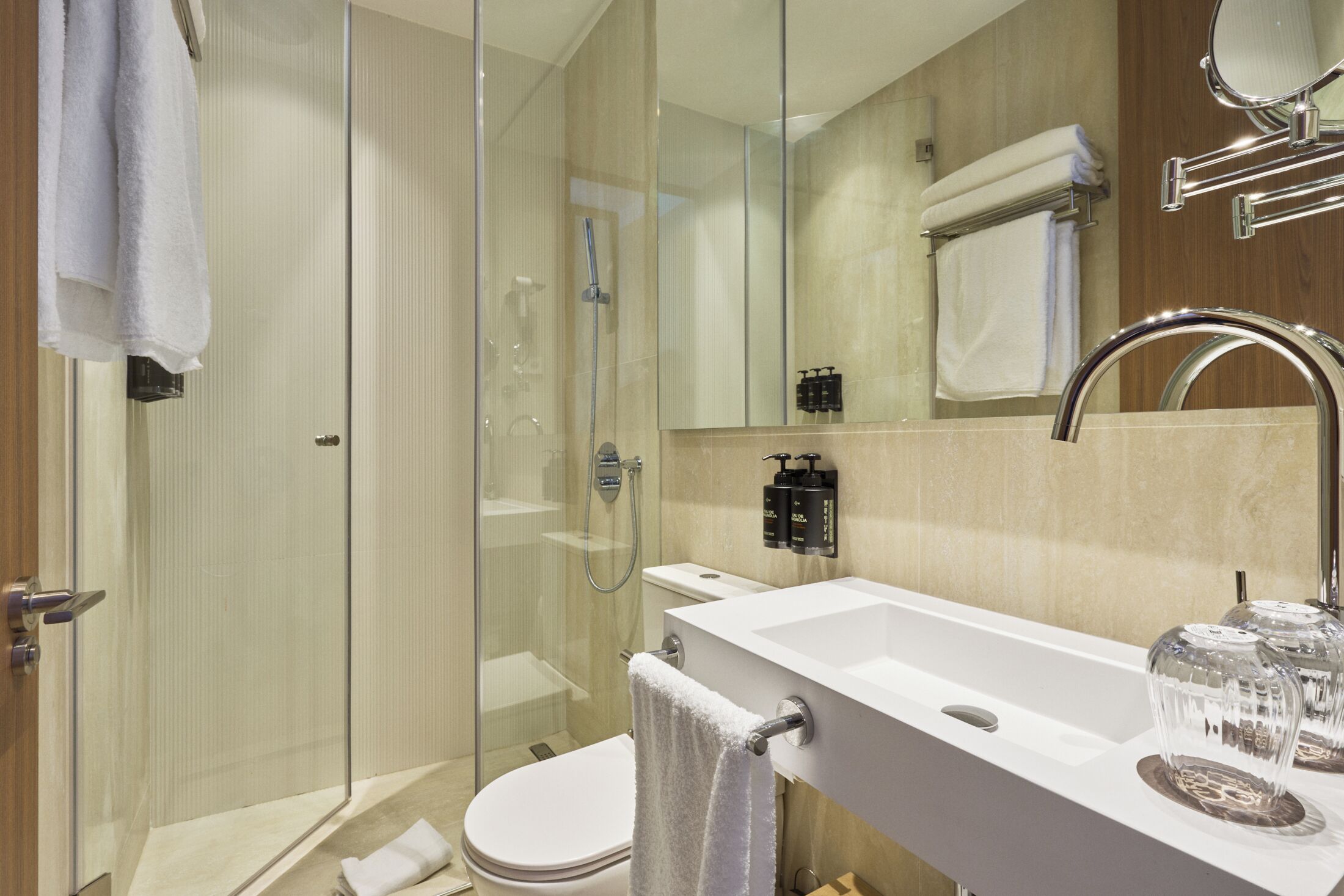 A modern bathroom with a glass shower enclosure, a white sink with a chrome faucet, and a large mirror above the sink.