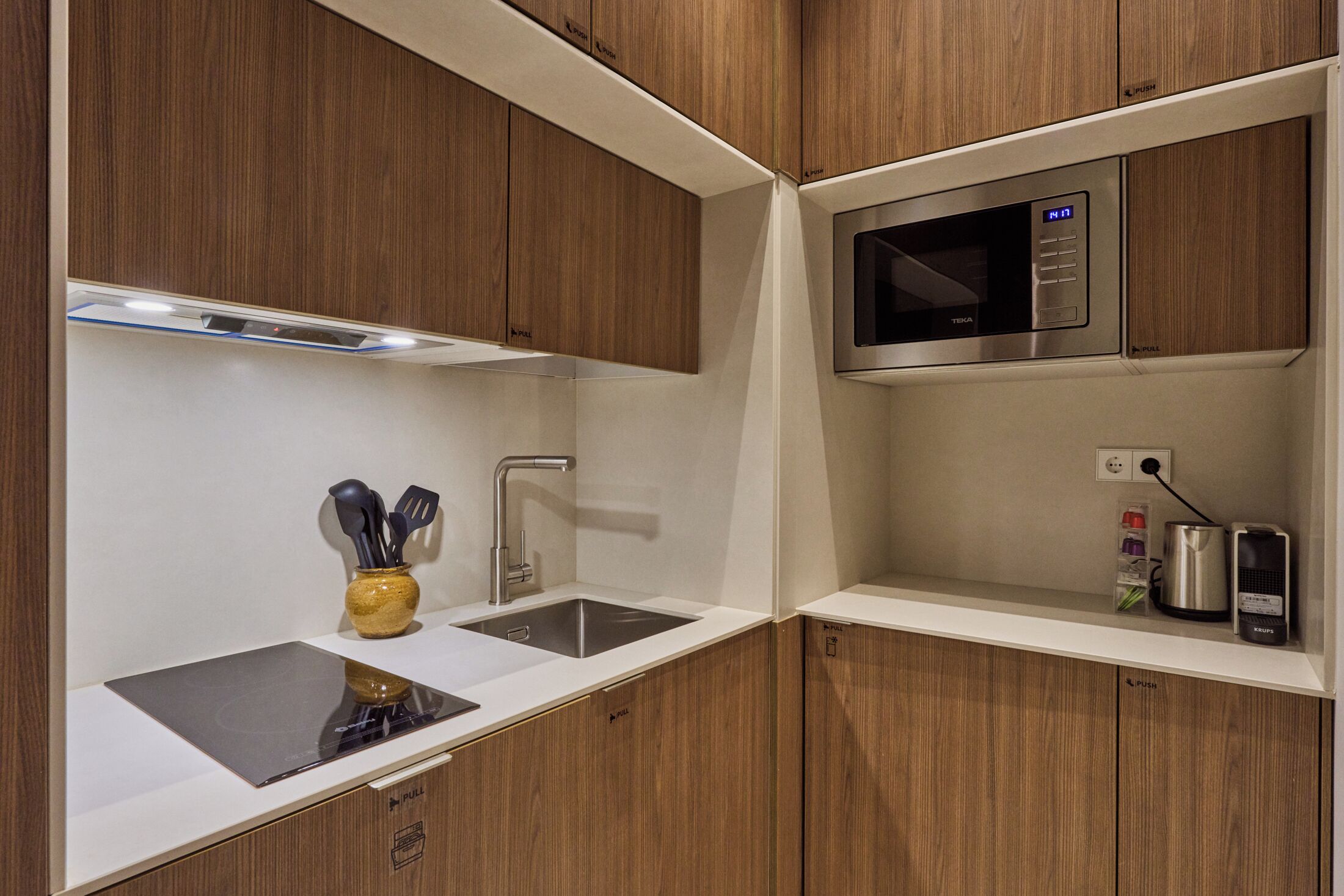 Una cocina moderna con armarios de madera, un lavamanos de acero inoxidable, un microondas y un hervidor.
