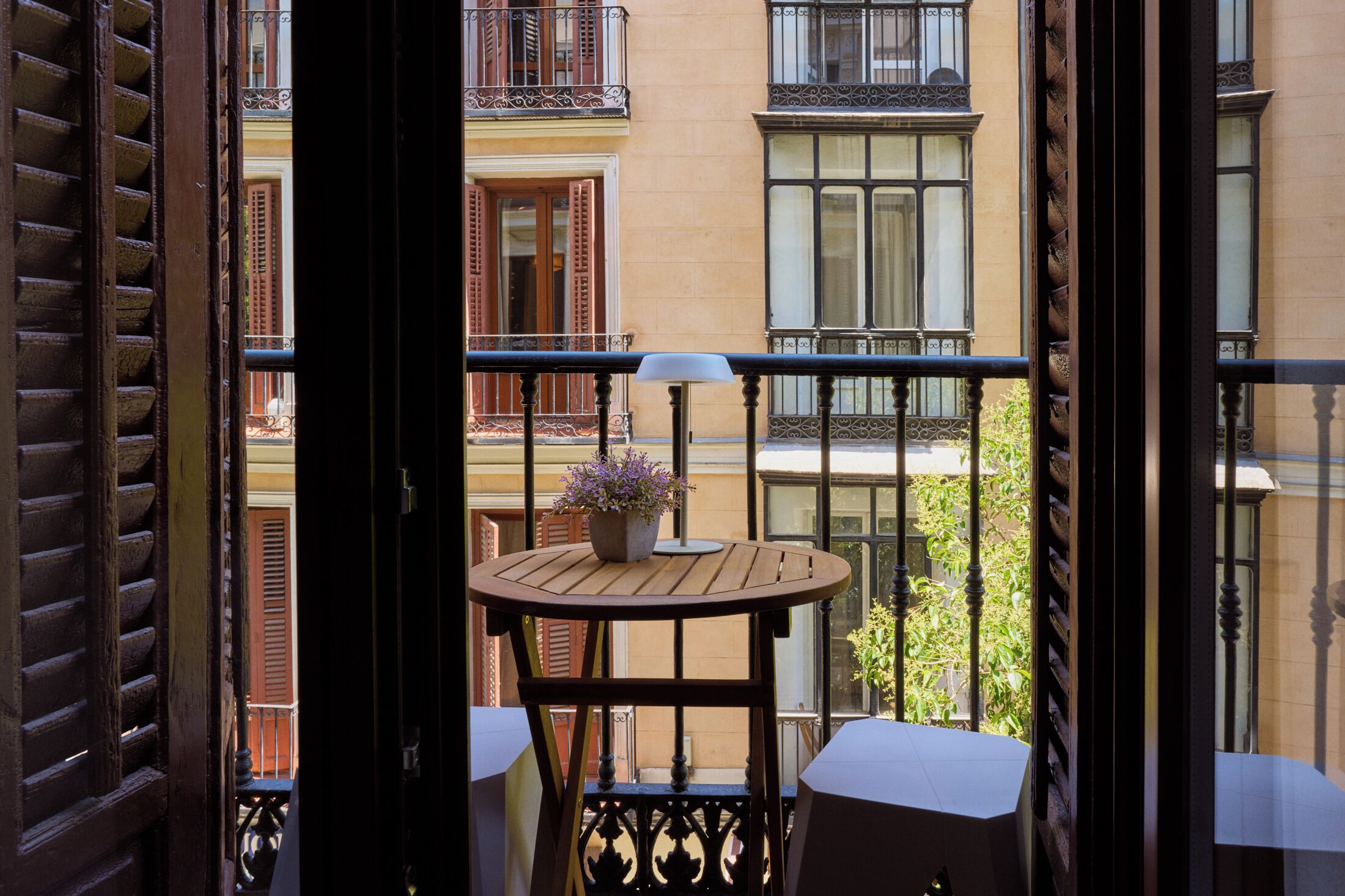 Een balkon met een houten tafel en stoelen, een potplant en uitzicht op omliggende gebouwen.