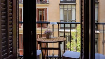 Een balkon met een houten tafel en stoelen, een potplant en uitzicht op omliggende gebouwen.
