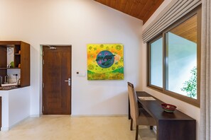 Um quarto com porta de madeira, mesa de jantar com cadeiras, janela com vista e um quadro pendurado na parede.