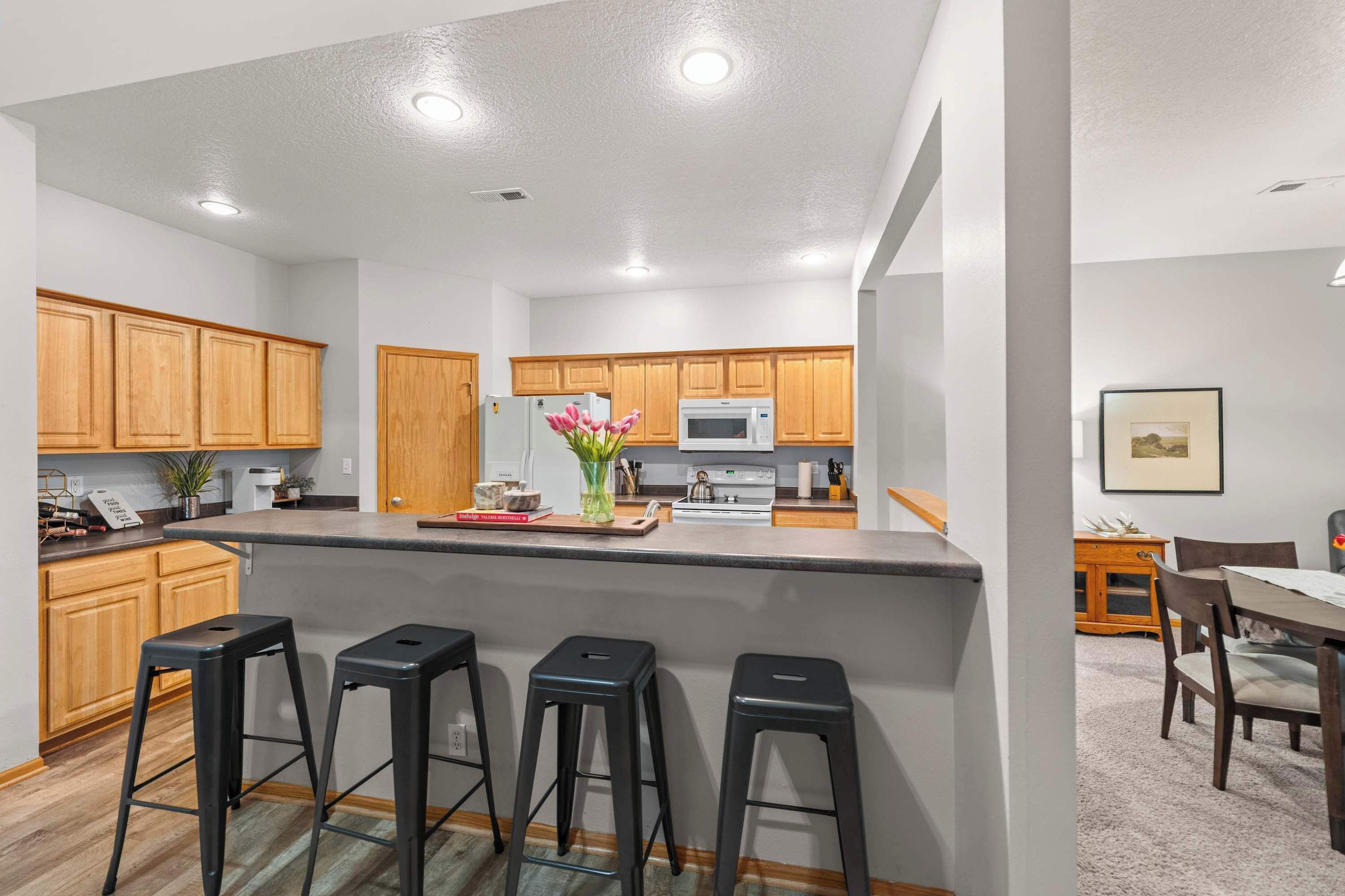 A modern kitchen with wooden cabinets, a central island with bar stools, a microwave, and a stove.