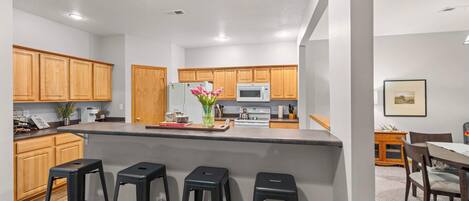 A modern kitchen with wooden cabinets, a central island with bar stools, a microwave, and a stove.