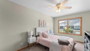 A bedroom with a bed, nightstands, a ceiling fan, and a window with a view of buildings.