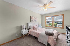 A bedroom with a bed, nightstands, a ceiling fan, and a window with a view of buildings.