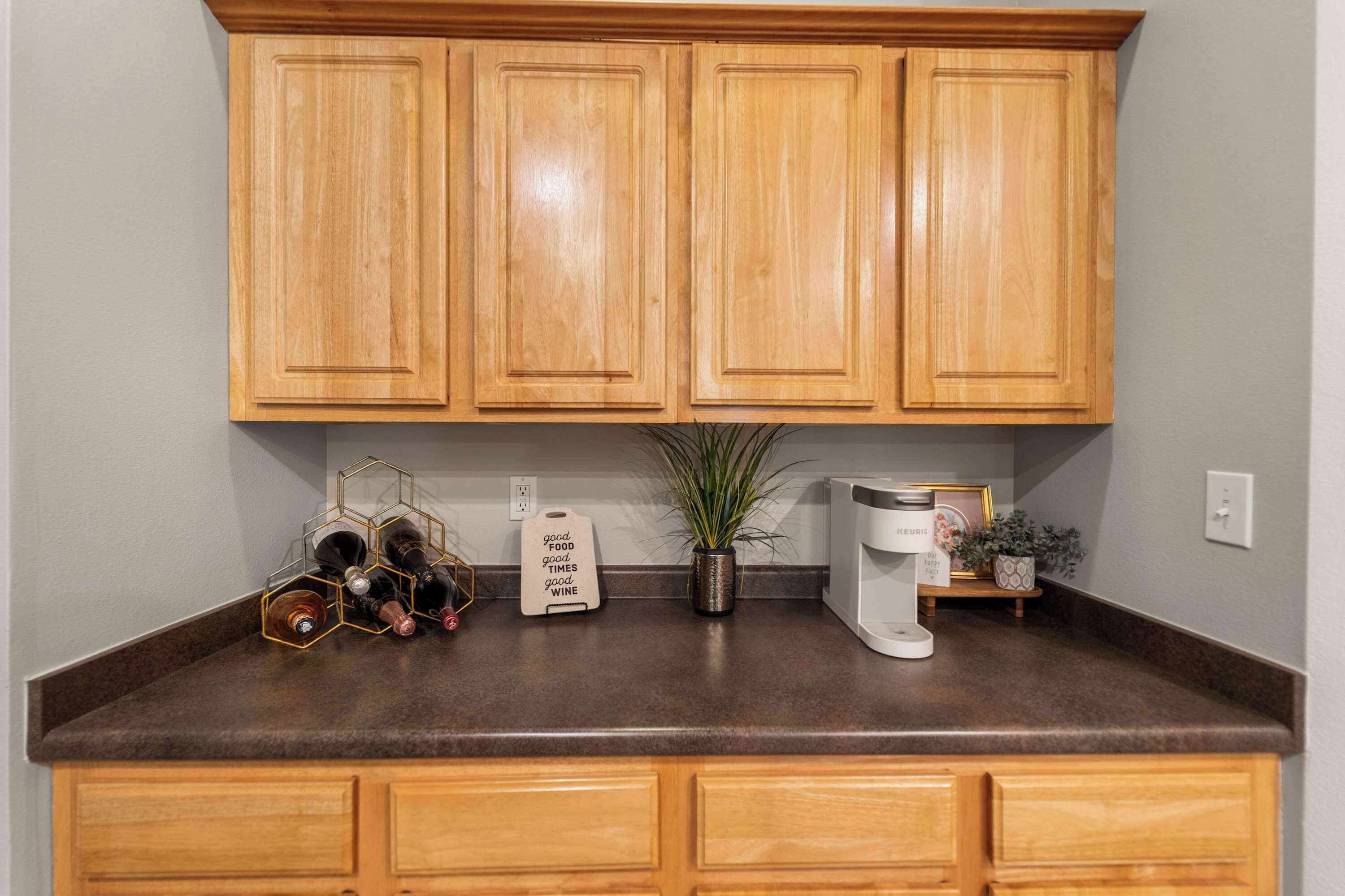 Cocina con armarios de madera, una encimera, una estantería para vinos, una cafetera y una planta en maceta.