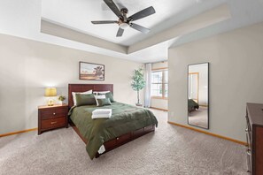 A bedroom with a bed, nightstand, lamp, ceiling fan, window, and a mirror.