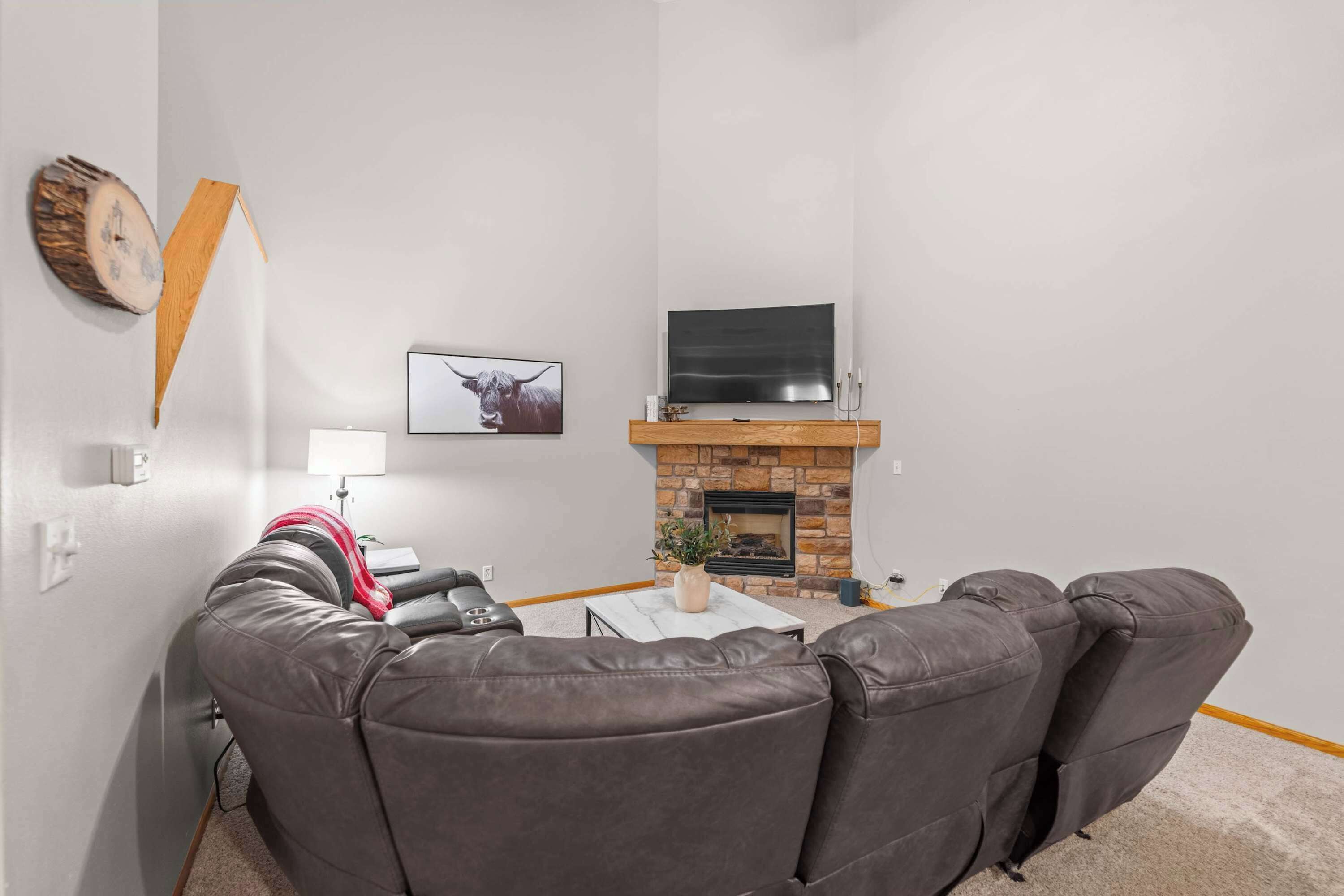 Un salon avec une cheminée, un téléviseur à écran plat, un canapé en cuir et un tableau accroché au mur.
