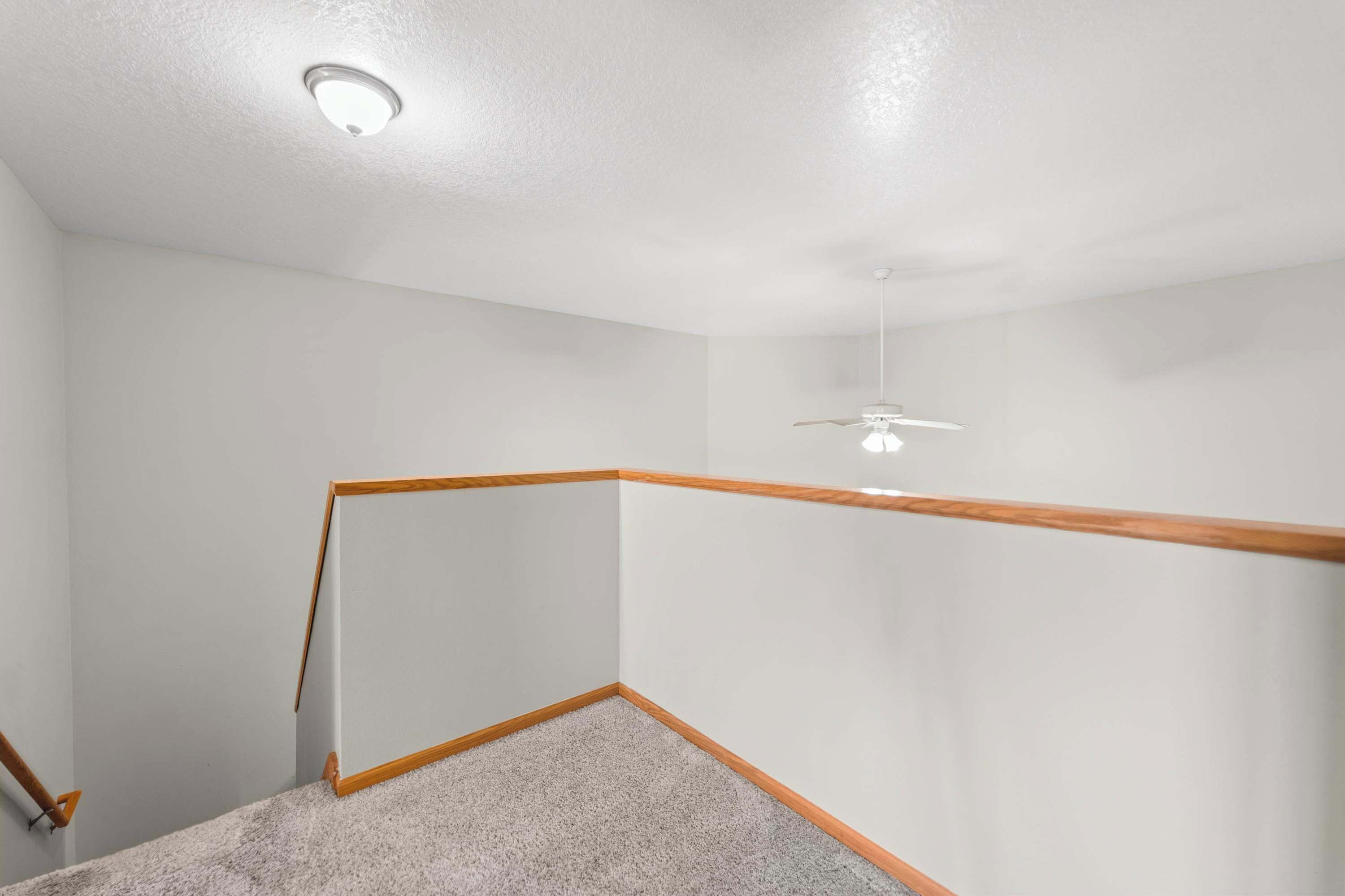 Une pièce avec un escalier en bois, un ventilateur de plafond et un sol recouvert de moquette.
