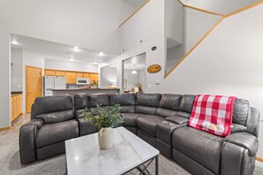 A modern living room with a sectional sofa, a marble coffee table, and a kitchen in the background.