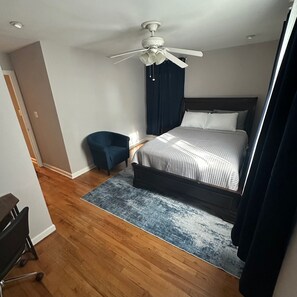 Ein Schlafzimmer mit einem Bett, einem Sessel, einem Deckenventilator und Holzboden.