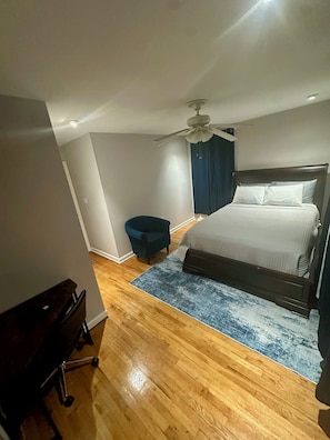 A bedroom with a bed, a ceiling fan, a blue chair, and a wooden floor. - Serene 3-Bedroom townhouse where location meets comfort and convenience. (Woodlawn)