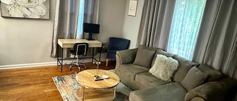 Un salon comprenant un canapé, une table basse, un bureau avec un ordinateur et un grand tableau représentant des fleurs accroché au mur.