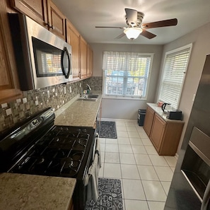 A kitchen with a stove, microwave, and ceiling fan. - Serene 3-Bedroom townhouse where location meets comfort and convenience. (Woodlawn)