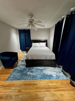 Ein Schlafzimmer mit einem Bett, einem Deckenventilator und einem blauen Vorhang.