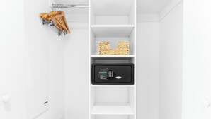 En vit garderob med en flätad korg på den översta hyllan och ett svart kassaskåp med ett digitalt knappsats på den nedre delen.