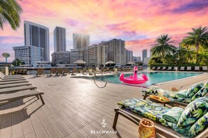 A rooftop pool with lounge chairs and a flamingo float, surrounded by tall buildings and palm trees. - Modern Stylish Studio - Beach Access + Resort Life (Hallandale Beach)
