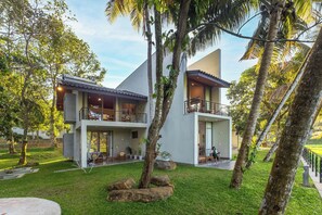 A modern two-story house with a balcony, surrounded by lush greenery and palm trees. - ONA Garden Villa: Deluxe Double/Twin Room (Galle)