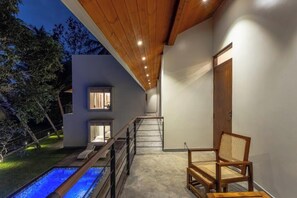 A modern outdoor area with a pool, a wooden chair, and a staircase leading to a second-floor balcony. - ONA Garden Villa: Deluxe Double/Twin Room (Galle)