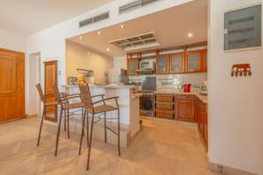 Una cocina con armarios de madera, microondas, estufa y comedor con sillas.