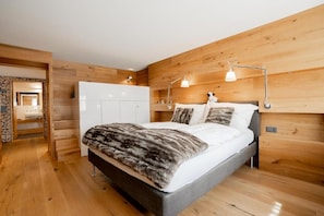 A bedroom with a bed, wooden walls, a white wardrobe, and a stone wall in the background. - Beaulieu - Inspiringplaces Zermatt (Zermatt)