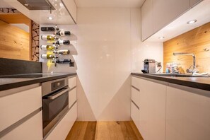 A modern kitchen with white cabinets, a wooden countertop, and a wine rack. - Beaulieu - Inspiringplaces Zermatt (Zermatt)