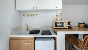 A compact kitchen with white cabinets, a built-in microwave, a small refrigerator, and a bar stool. - Studio in Pigalle - Moulin Rouge and Montmartre (Paris)