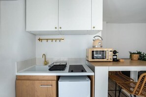 Eine kompakte Küche mit weißen Schränken, einer eingebauten Mikrowelle, einem kleinen Kühlschrank und einem Barhocker.