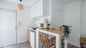 A compact kitchen with white cabinetry, a microwave, and a small dining table with wicker chairs. - Studio in Pigalle - Moulin Rouge and Montmartre (Paris)