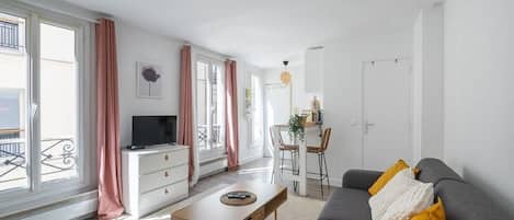 A modern living room with a sofa, a coffee table, a TV, and a dining area with chairs and a table.