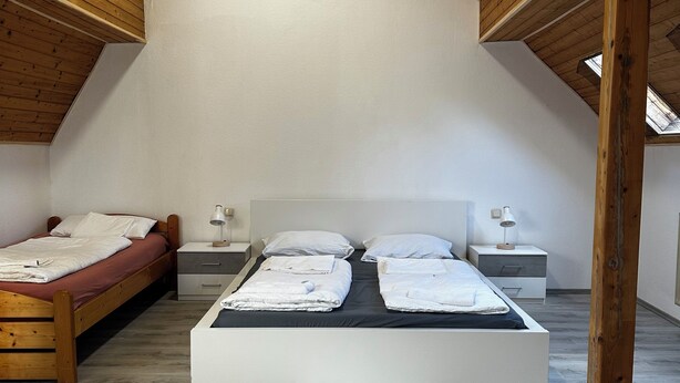 A bedroom with a sloped ceiling, wooden beams, a large bed, bedside tables, and a skylight.