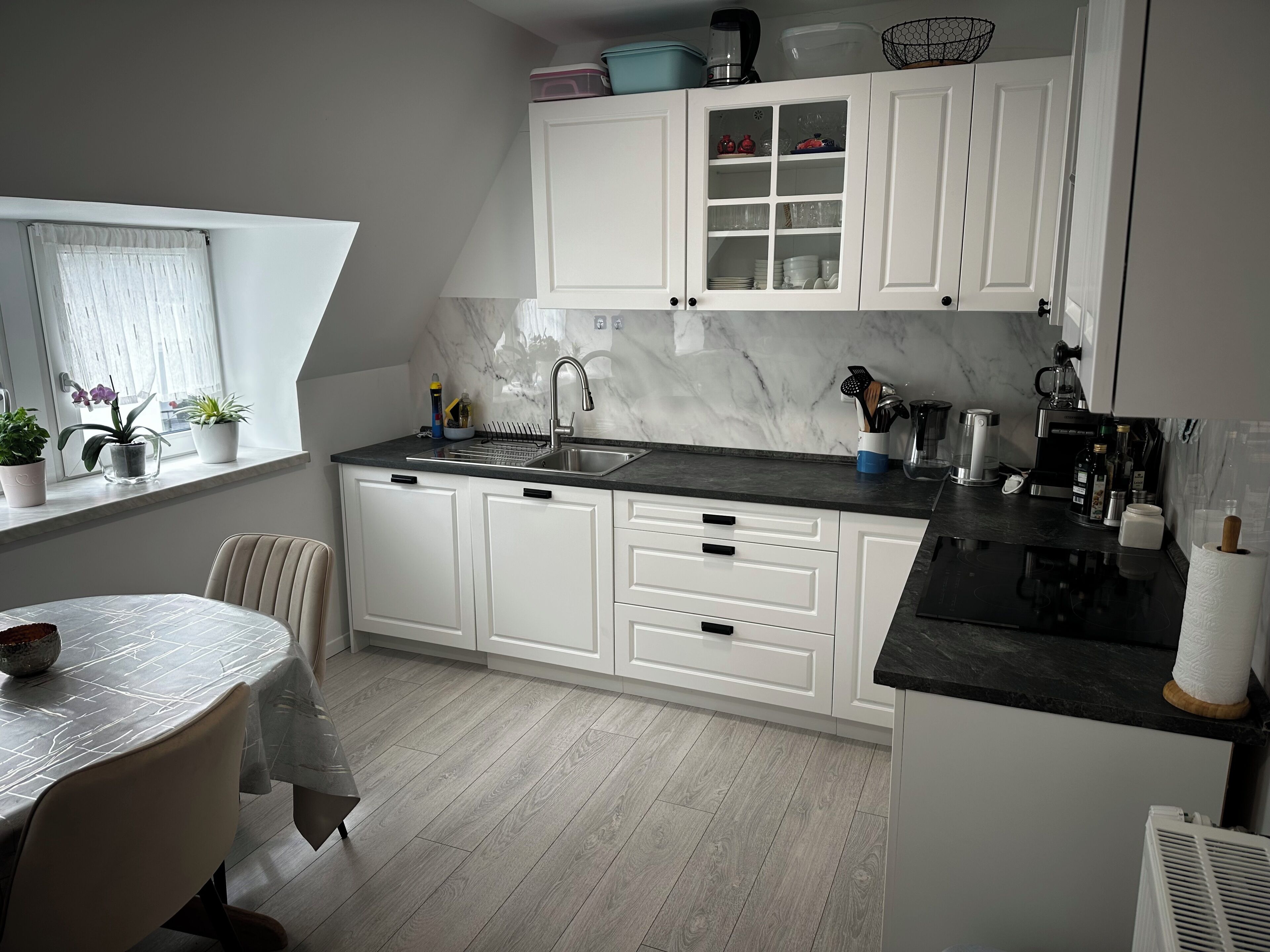 Una cocina moderna con armarios blancos, encimera negra y una zona de comedor con mesa y sillas.