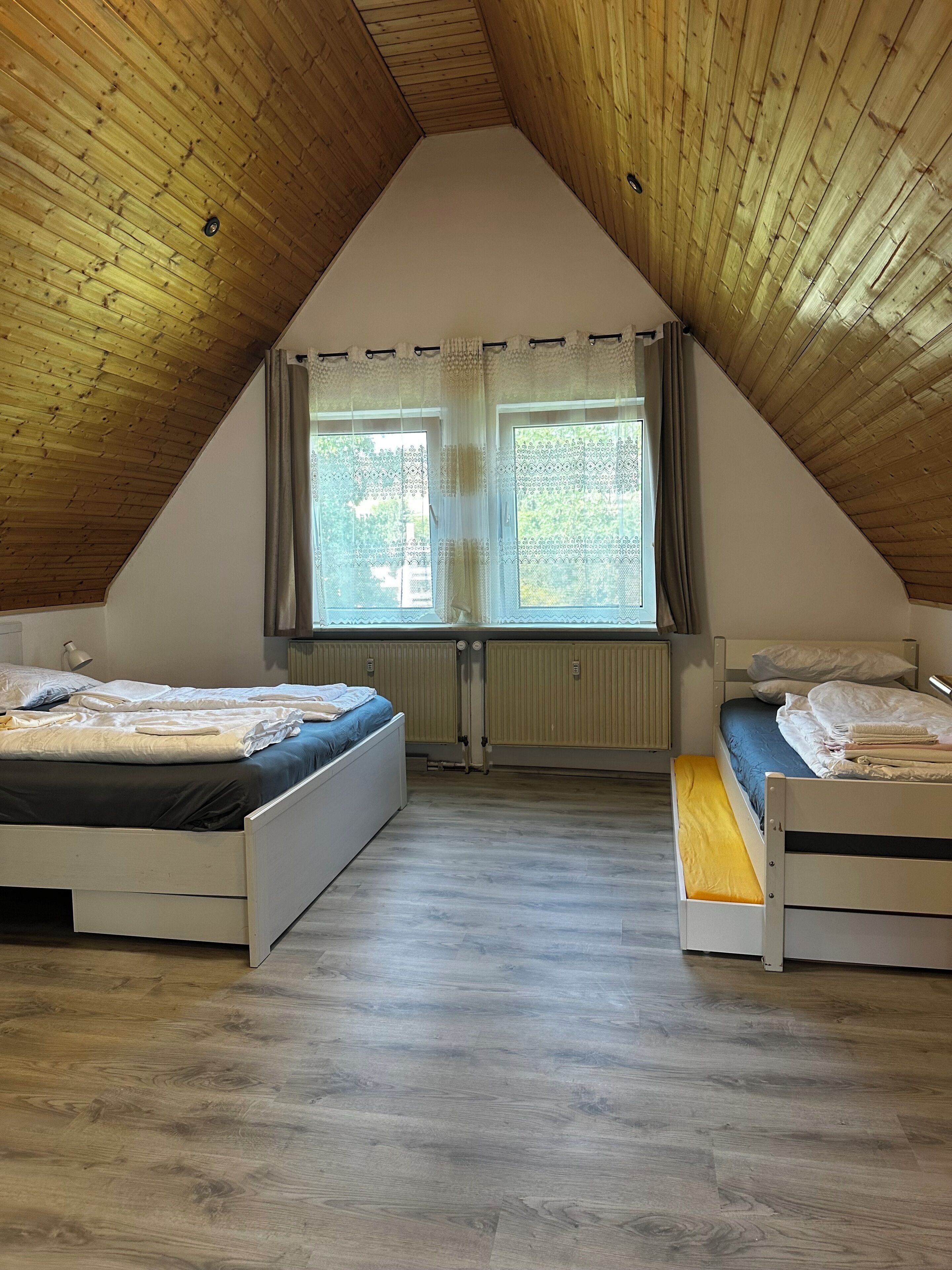 A room with two beds, a sloped ceiling, and a window with curtains.