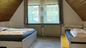 A room with two beds, a sloped ceiling, and a window with curtains.