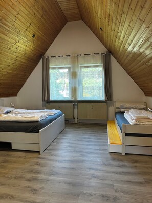 Une chambre avec deux lits, un plafond en pente et une fenêtre avec des rideaux.
