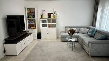 Ein modernes Wohnzimmer mit Fernseher, einem grauen Sofa, einem weißen Schrank und einem Glastisch.