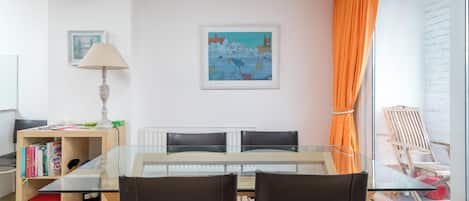 Un salon moderne avec une table à manger en verre, deux chaises, une bibliothèque, une lampe et un tableau accroché au mur.