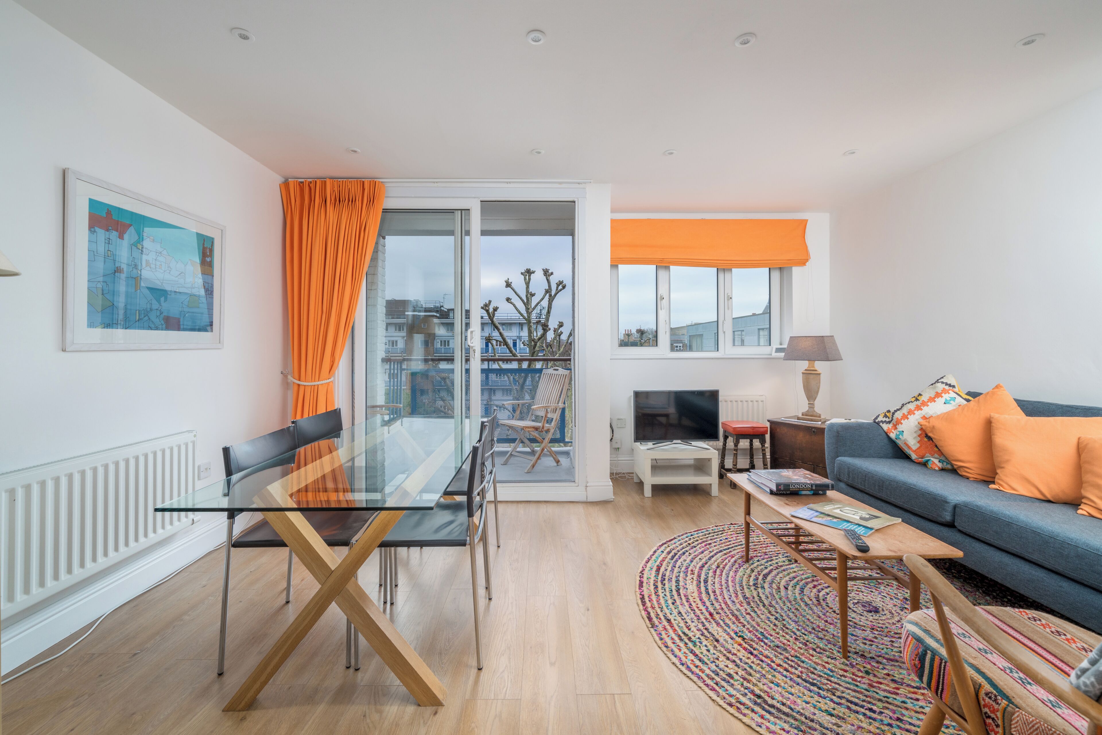 A modern living room with a glass dining table, a sofa, and a view of the city.